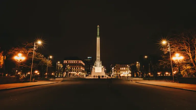 Brīvības piemineklis Rīgā naktī, izgaismots ar siltu apgaismojumu tumšajās ielās.