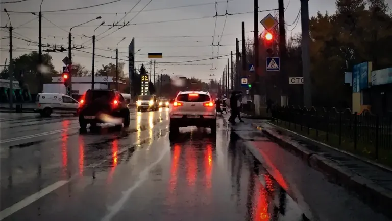Automašīnas brauc pa slapju un lietainu pilsētas ielu agrā rīta stundā Latvijā.