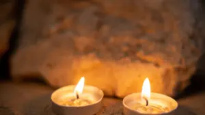 Divas degošas tējas sveces uz smilšainas virsmas ar neasu akmeni fonā tumšā vidē.