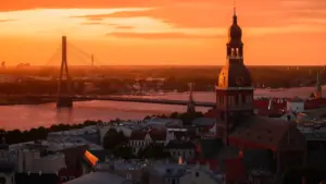 Panorāmas skats uz Rīgu un Vanšu tiltu saulrietā pār Daugavas upi.