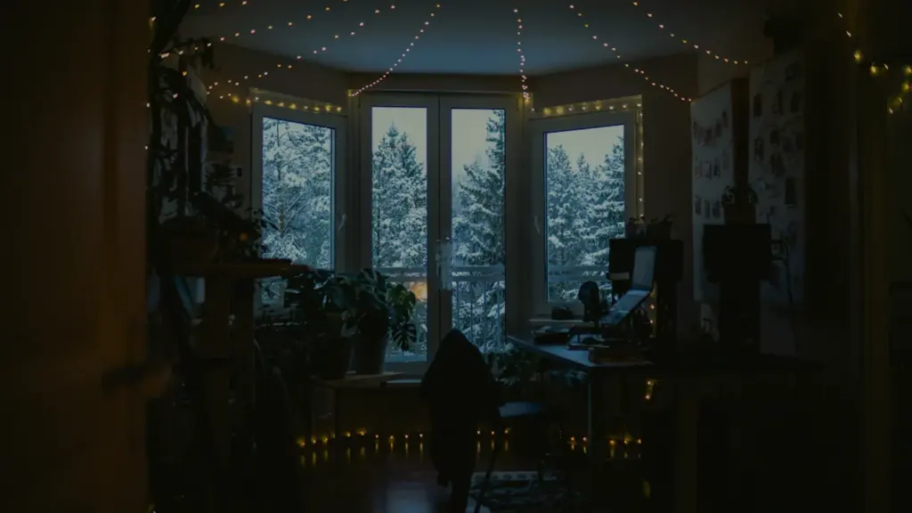 Mājīga istaba ar gaismas virtenēm un skatu uz sniegotu ziemas vakaru aiz loga