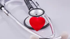 Sarkana sirds uz medicīniskā stetoskopa uz balta fona, simbolizējot sirds veselību.