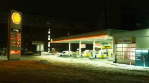 Degvielas uzpildes stacija naktī ar sniegu, atspoguļojot degvielas cenu mainīgumu Latvijas ziemas apstākļos.