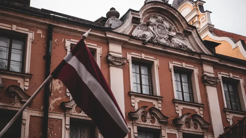 Latvijas karogs plīvo pie vēsturiskas ēkas Vecrīgā, simbolizējot valsts neatkarību un Atmodas laiku.
